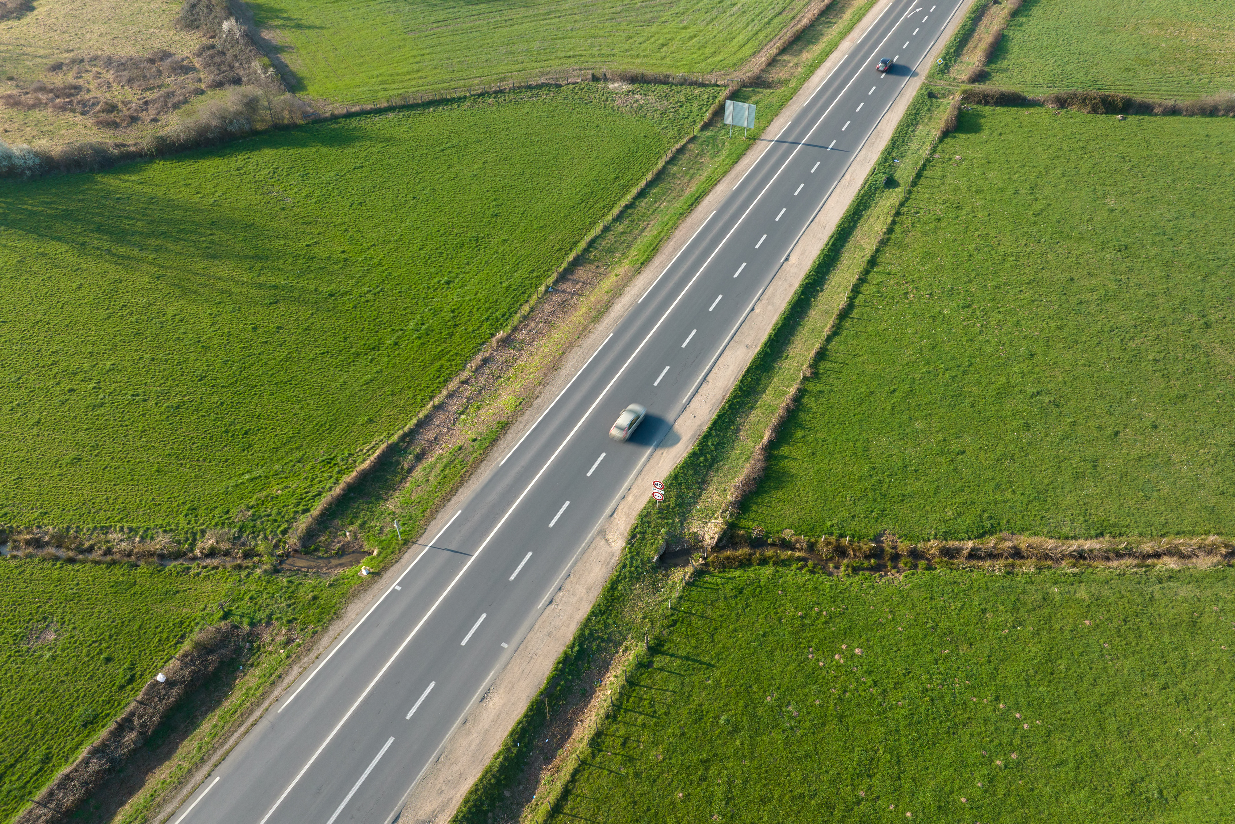 Aerial view of intercity road between green agricultural fields with fast driving cars. Top view from drone of highway traffic - Safe Travels VIP