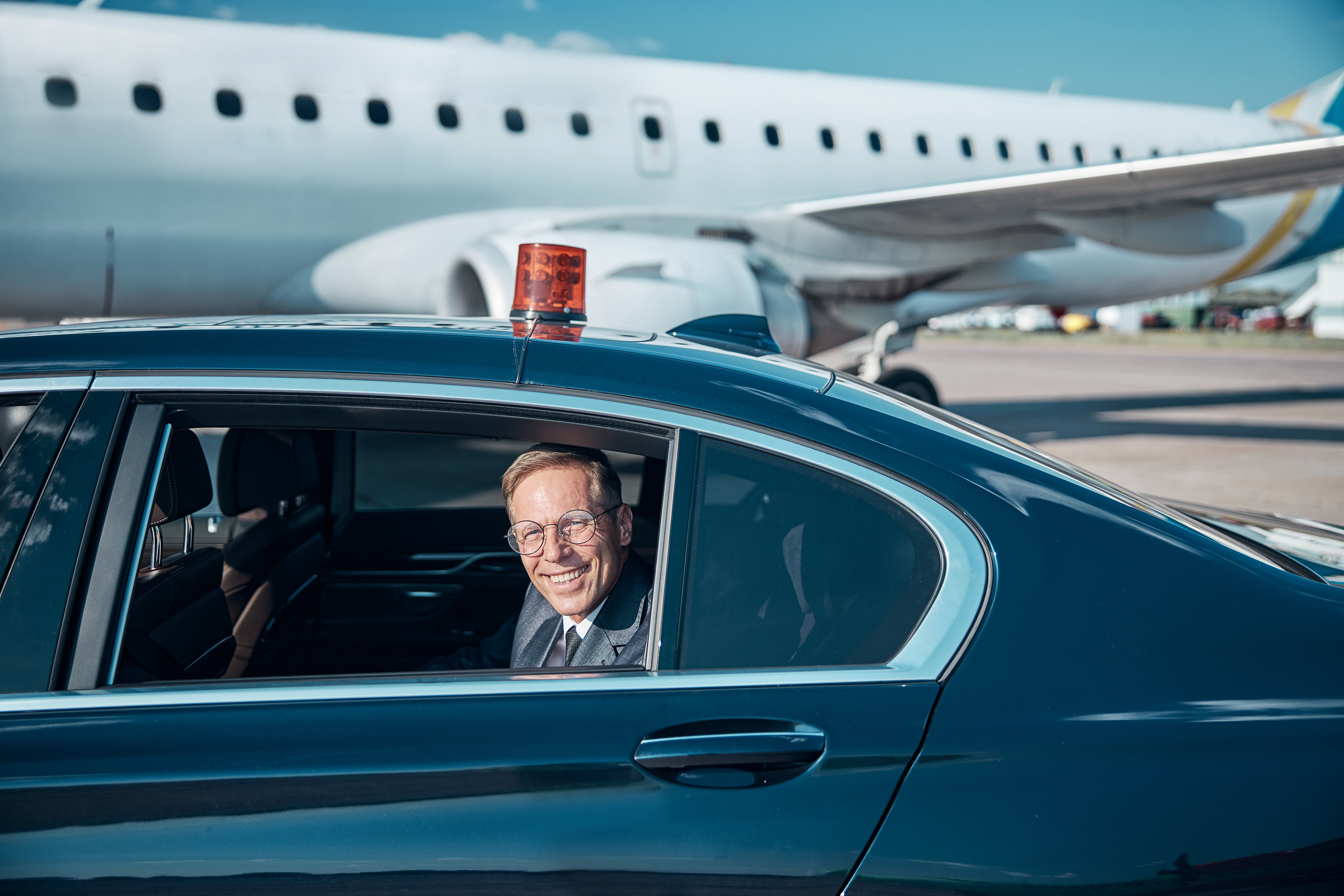Smiling Man Sits in Car Near an Airplane, Gatwick Airport UK - Safe Travels VIP